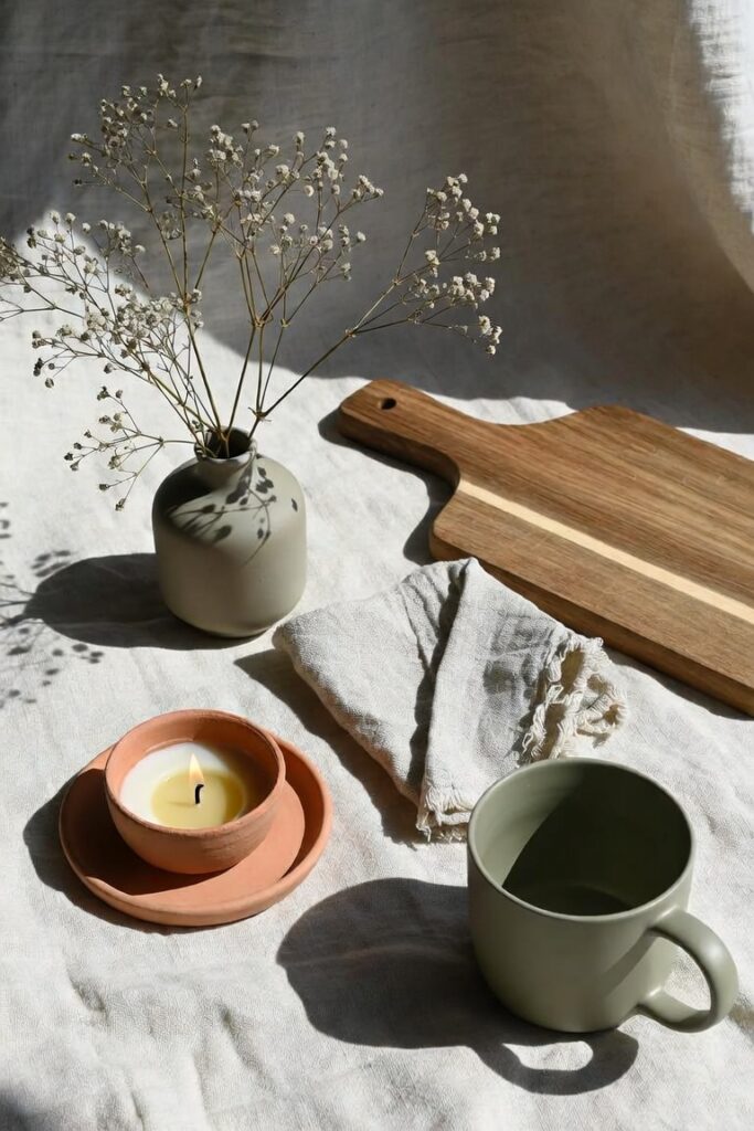 flat lay of budget kitchen decor items including ceramic vase wooden cutting board linen napkin and terracotta candle on cream linen surface