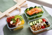Grab-and-go high-protein lunch meal prep containers with chicken burrito bowl, salmon and quinoa bowl, and Mediterranean chickpea bowl next to a canvas lunch tote