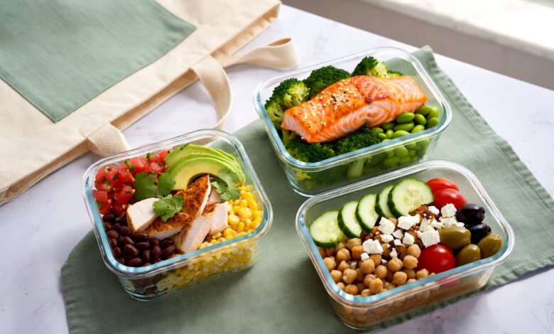 Grab-and-go high-protein lunch meal prep containers with chicken burrito bowl, salmon and quinoa bowl, and Mediterranean chickpea bowl next to a canvas lunch tote