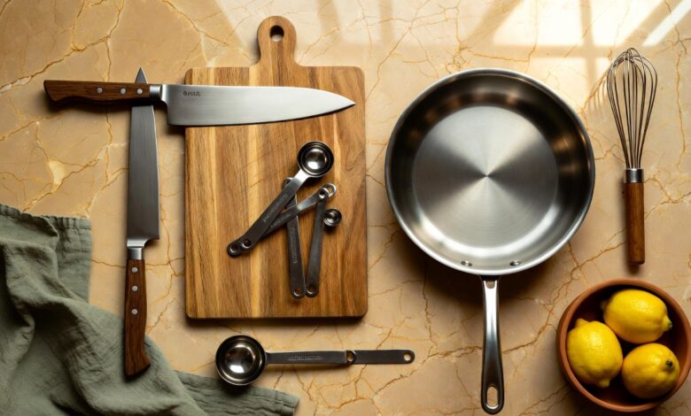 Flat lay of a chef's knife, cutting board, skillet, whisk, and measuring spoons on a marble counter with a bowl of lemons
