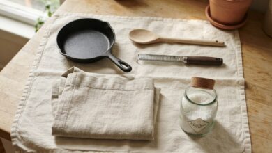 A flat lay of kitchen gifts on cream linen including a cast iron skillet, wooden spoon and zester